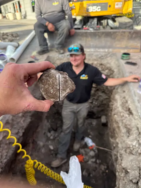 Element plumber holding broken pipe pulled from a sewer excavation