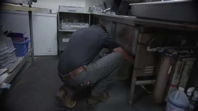 Plumber servicing water filters under a commercial kitchen sink