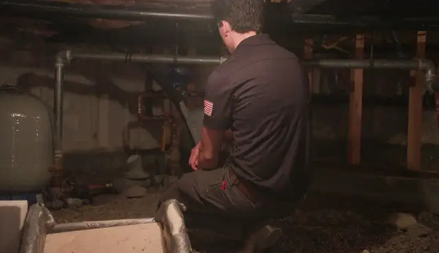 Plumber working in a crawl space beside a well pressure tank