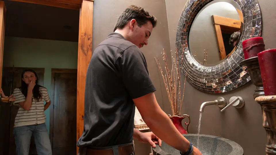 Plumber checking water flow at a bathroom faucet with the homeowner