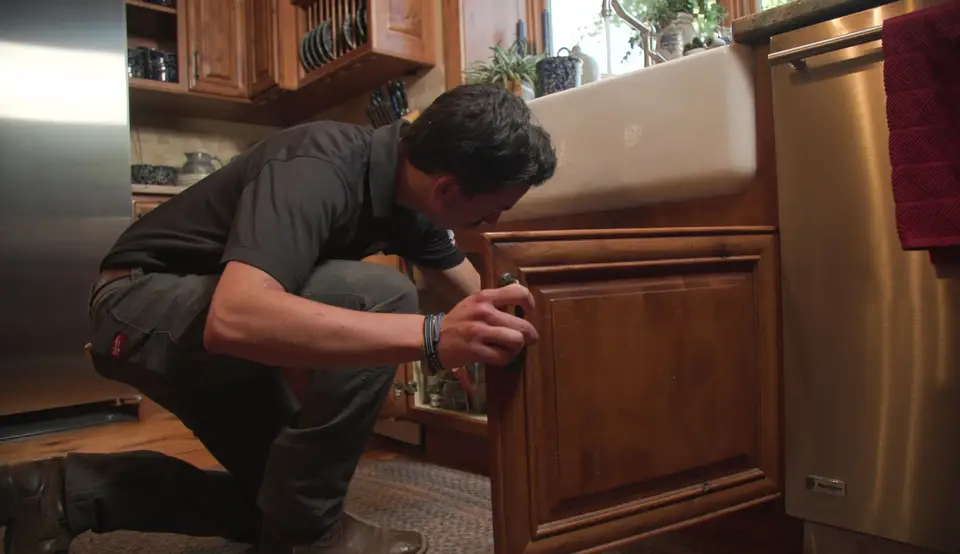 Plumber opening the cabinet under a kitchen farmhouse sink