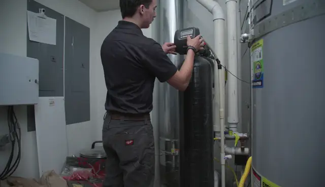 Technician adjusting a water softener in a mechanical room beside the water heater