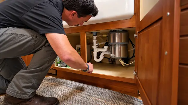 Element plumber inspecting under-sink plumbing and a garbage disposal