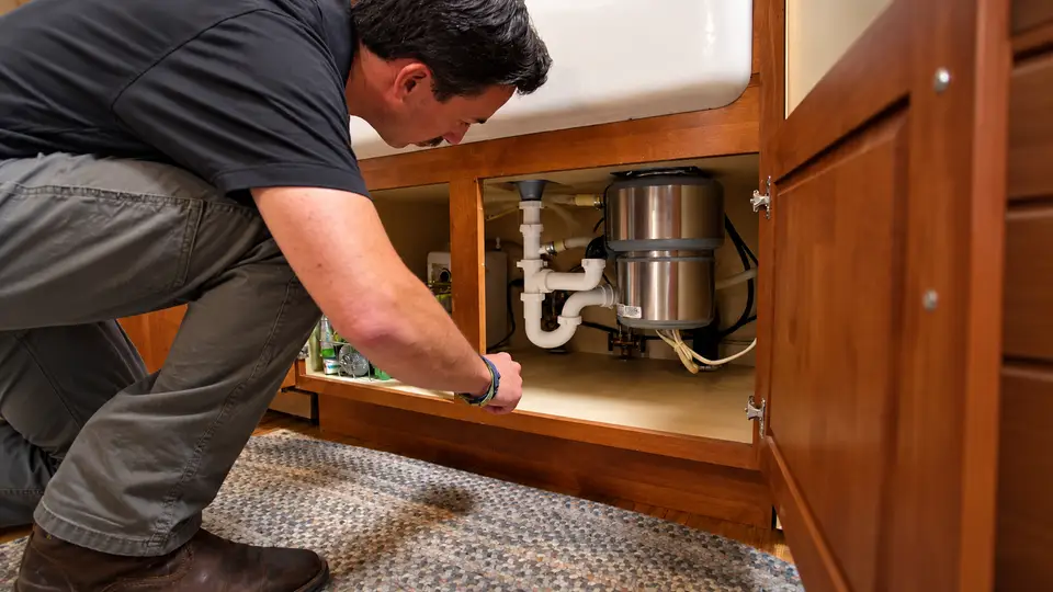 Element plumber inspecting under-sink plumbing and a garbage disposal
