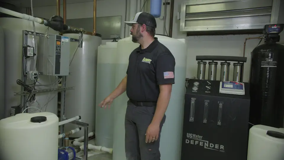 Technician walking through a water treatment room with storage tanks and filters